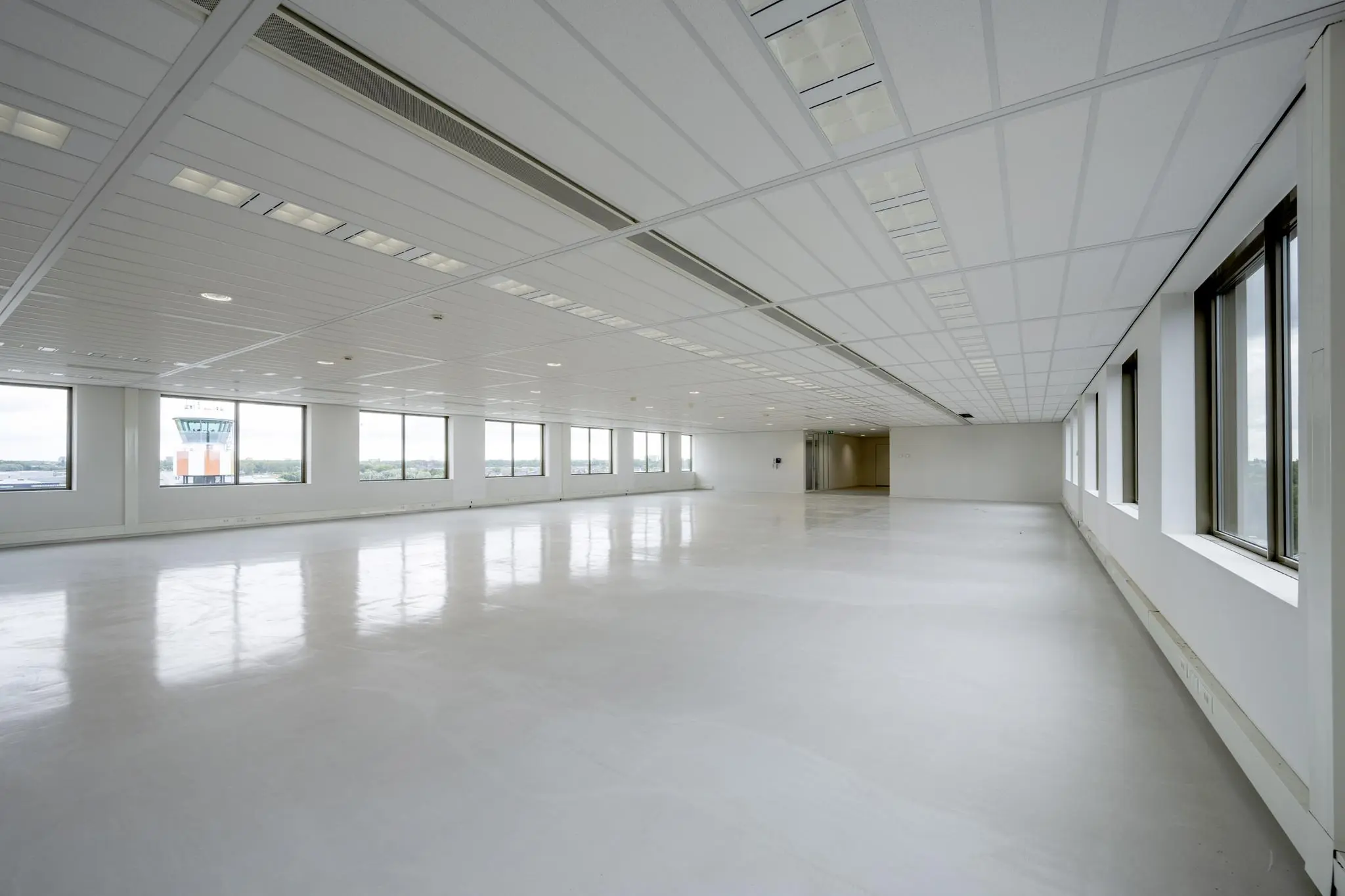 Lichte, lege kantoorruimte met uitzicht op de verkeerstoren van Rotterdam The Hague Airport.